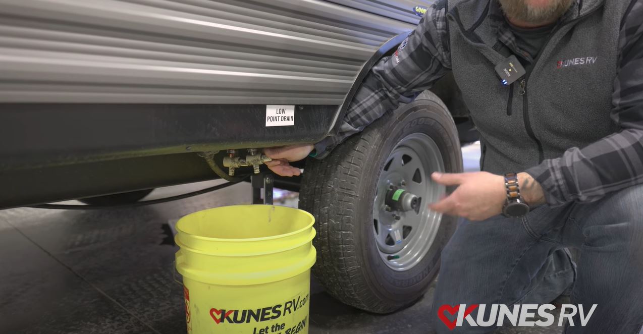picture of Kunes RV employee draining the water outside of an RV into a yellow Kunes RV bucket.