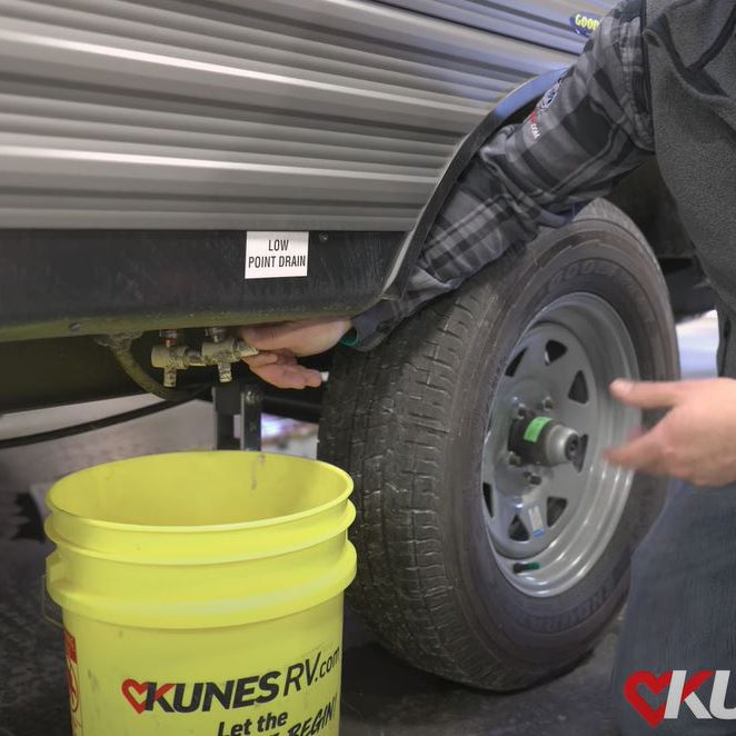 picture of Kunes RV employee draining the water outside of an RV into a yellow Kunes RV bucket.